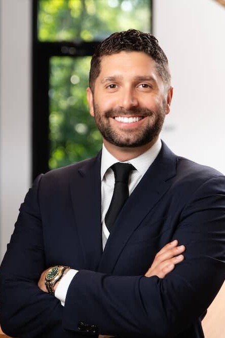 Smiling dark haired man with beard wearing suit with arms crossed