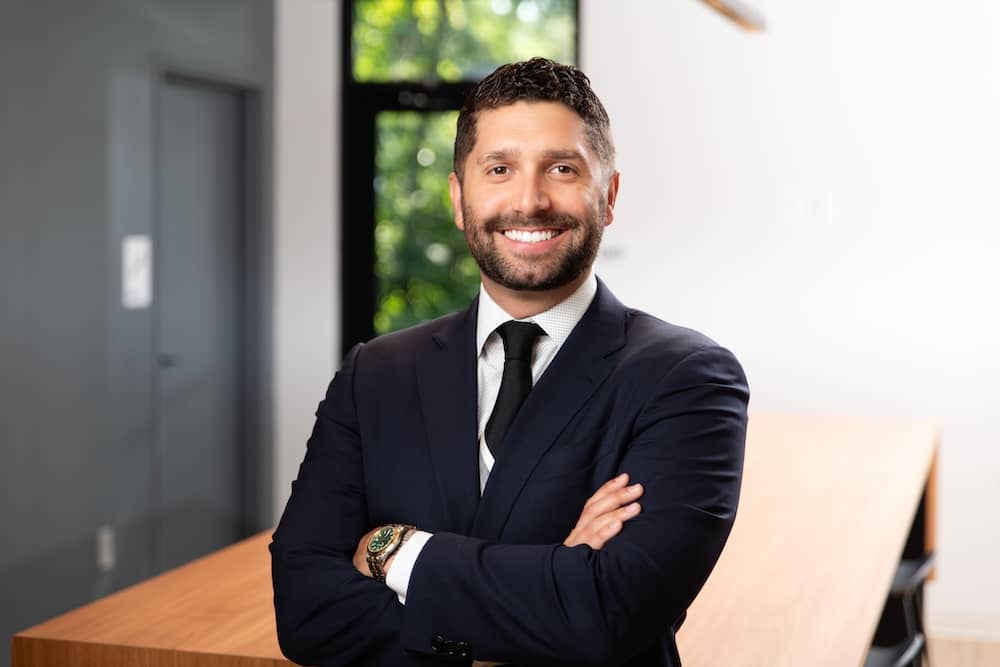 Smiling dark haired man with beard wearing suit with arms crossed