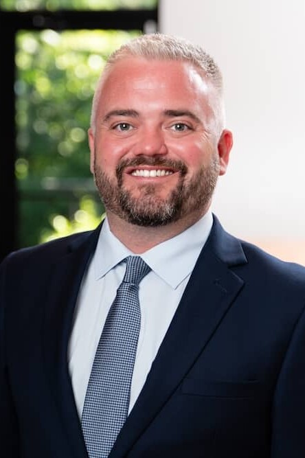 Smiling gray haired man with short beard wearing suit with blue tie